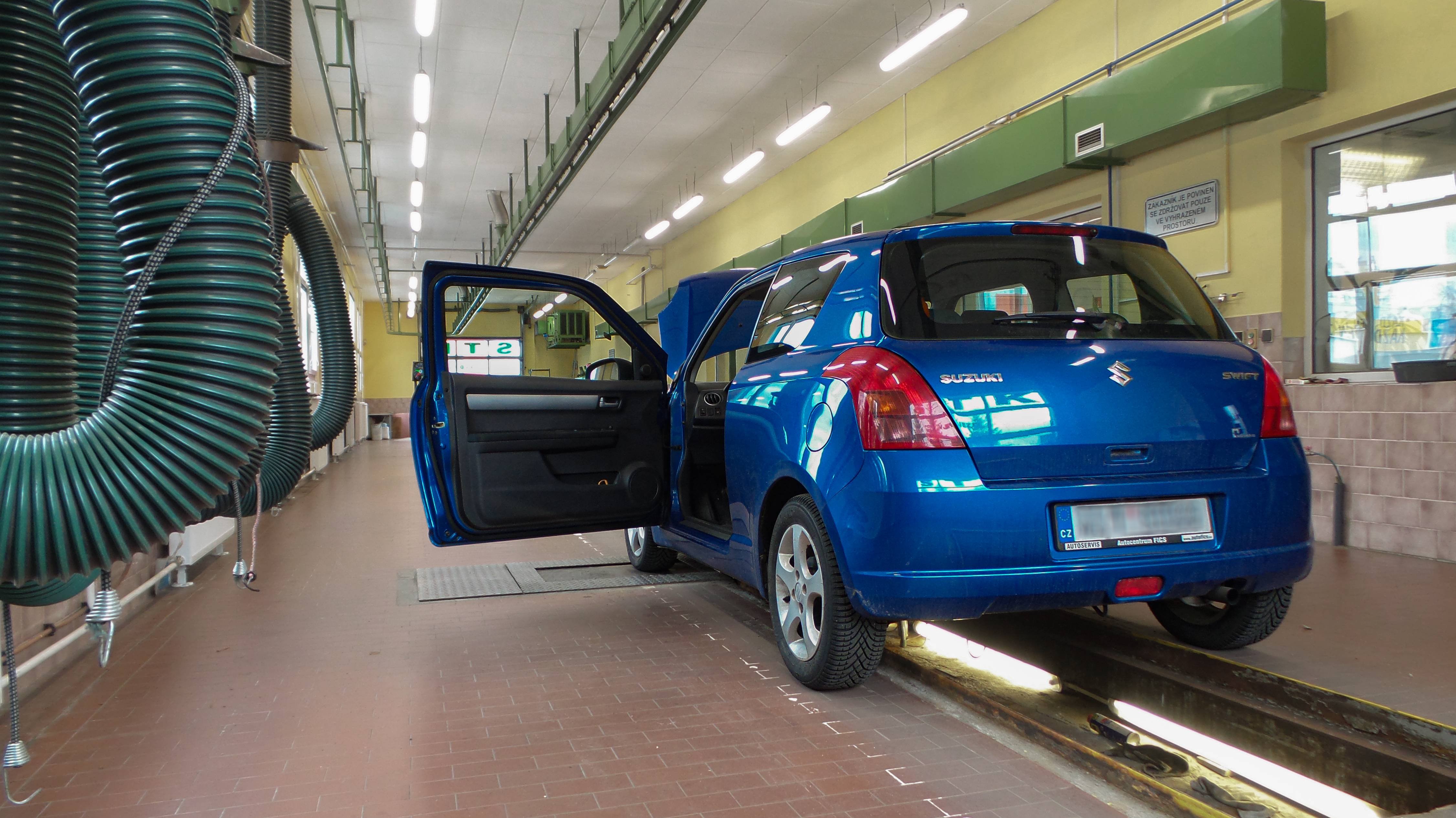Pohled na pracovní linku STK od vjezdu s modrým autem, které má otevřené dveře